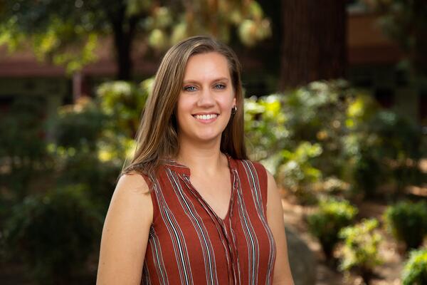 Headshot of Dr. Amanda Rupiper wearing a rust-colored blouse, smiling against a green outdoorsy background.