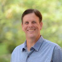 A headshot of Dr. David Cocker wearing a blue patterned button-down shirt